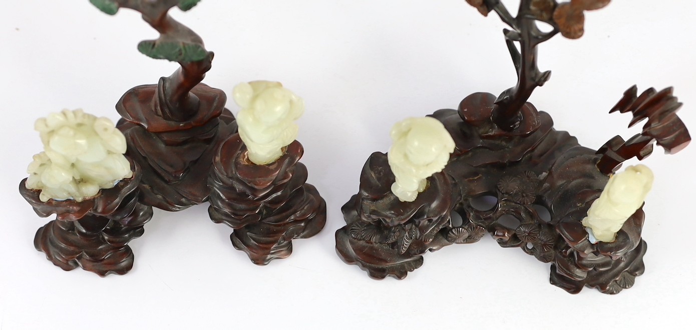 An assembled group of four Chinese pale celadon jade figures, 18th/19th century, displayed on two later wood 'rock-work' stands, total height approximately 19cm high